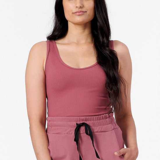 a woman wearing a ribbed pink tank top with a low scoop neck line. 