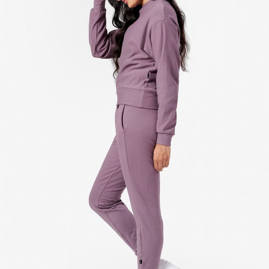 side of a woman wearing purple joggers and purple crew neck sweater