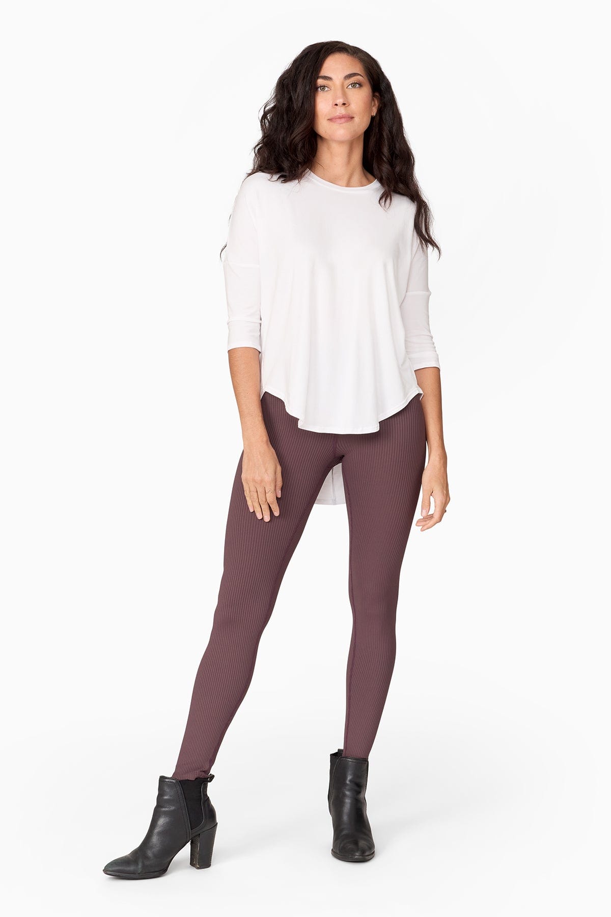 Woman wearing a 3/4 white shirt that is longer at the back. Paired with a brownish purple  legging and accessorized with a pointy black heel