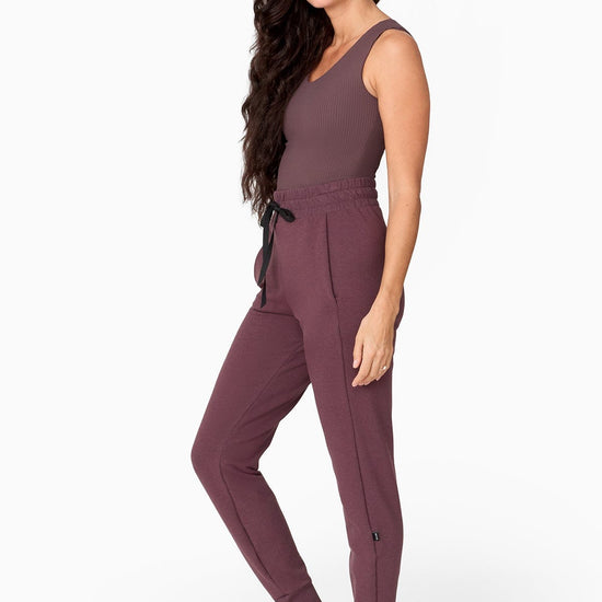a woman with waist length hair wears a brownish sleeveless tank with a matching colour full length jogger pant