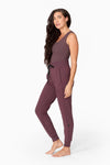 a woman with waist length hair wears a brownish sleeveless tank with a matching colour full length jogger pant