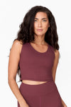 woman with long wavy brown hair wears a muted brownish/purple ribbon tank top