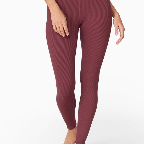 A tall woman wears a reddish purple fitted tank top with a matching legging.
