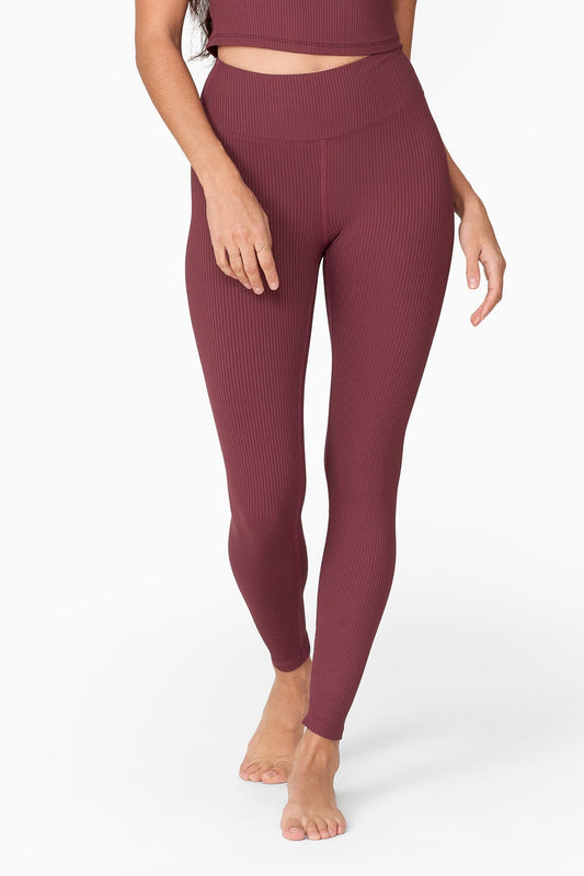 A tall woman wears a reddish purple fitted tank top with a matching legging.