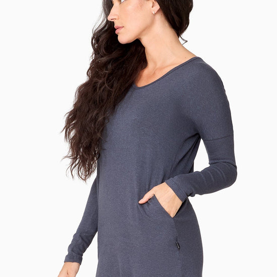 The side of a woman wearing a blue long sleeve sweater with pocket.