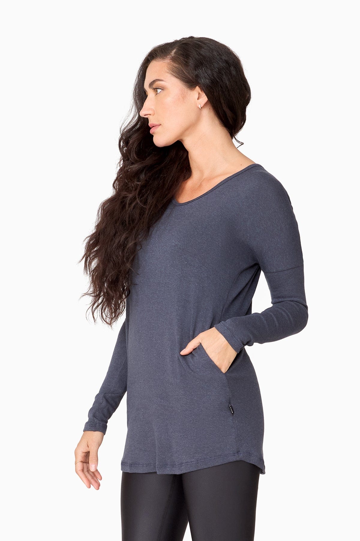 The side of a woman wearing a blue long sleeve sweater with pocket.