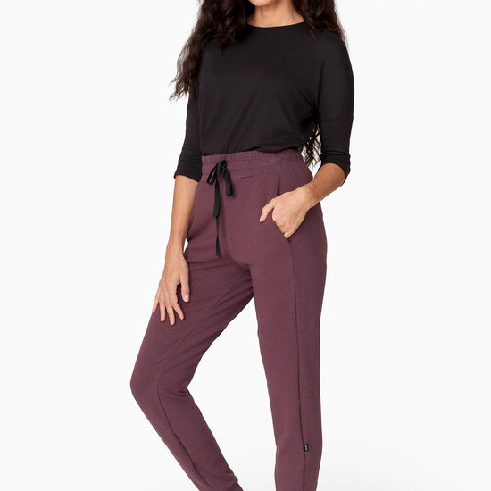 a woman with brunette wavy hair wears a 3/4 sleeve black shirt with a brownish purple jogger pant