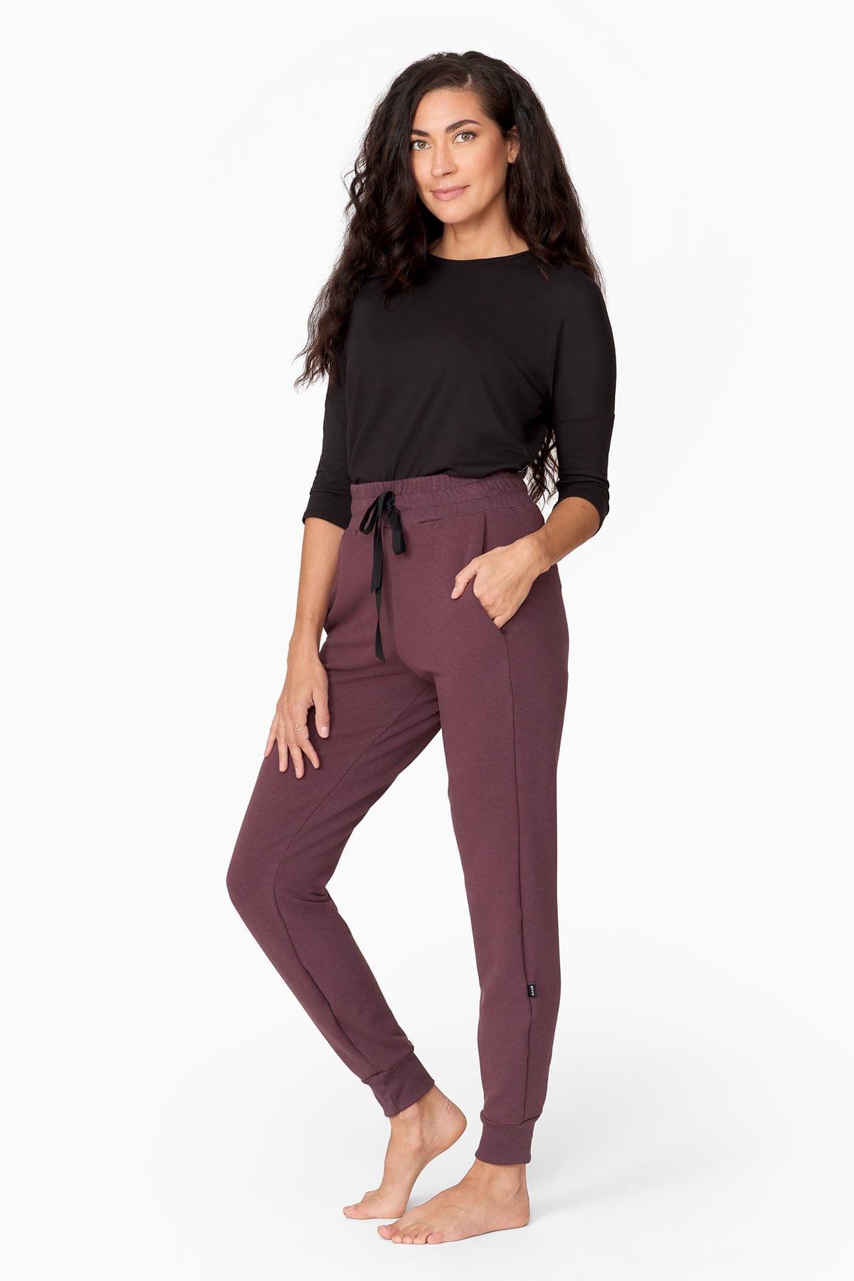 a woman with brunette wavy hair wears a 3/4 sleeve black shirt with a brownish purple jogger pant