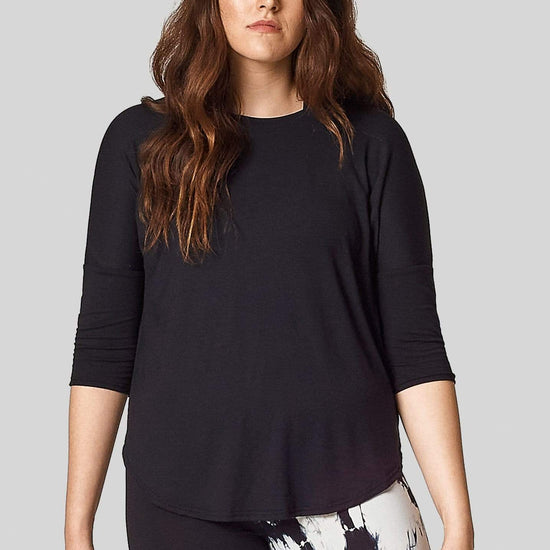 A model wears a t-shirt with 3/4 length sleeves in black with a hi-lo hem (longer in the back).