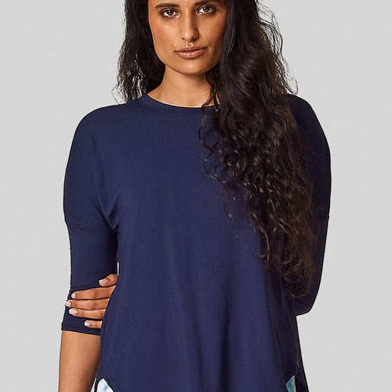 A woman wears a navy teeshirt with 3/4 length sleeves and printed leggings.