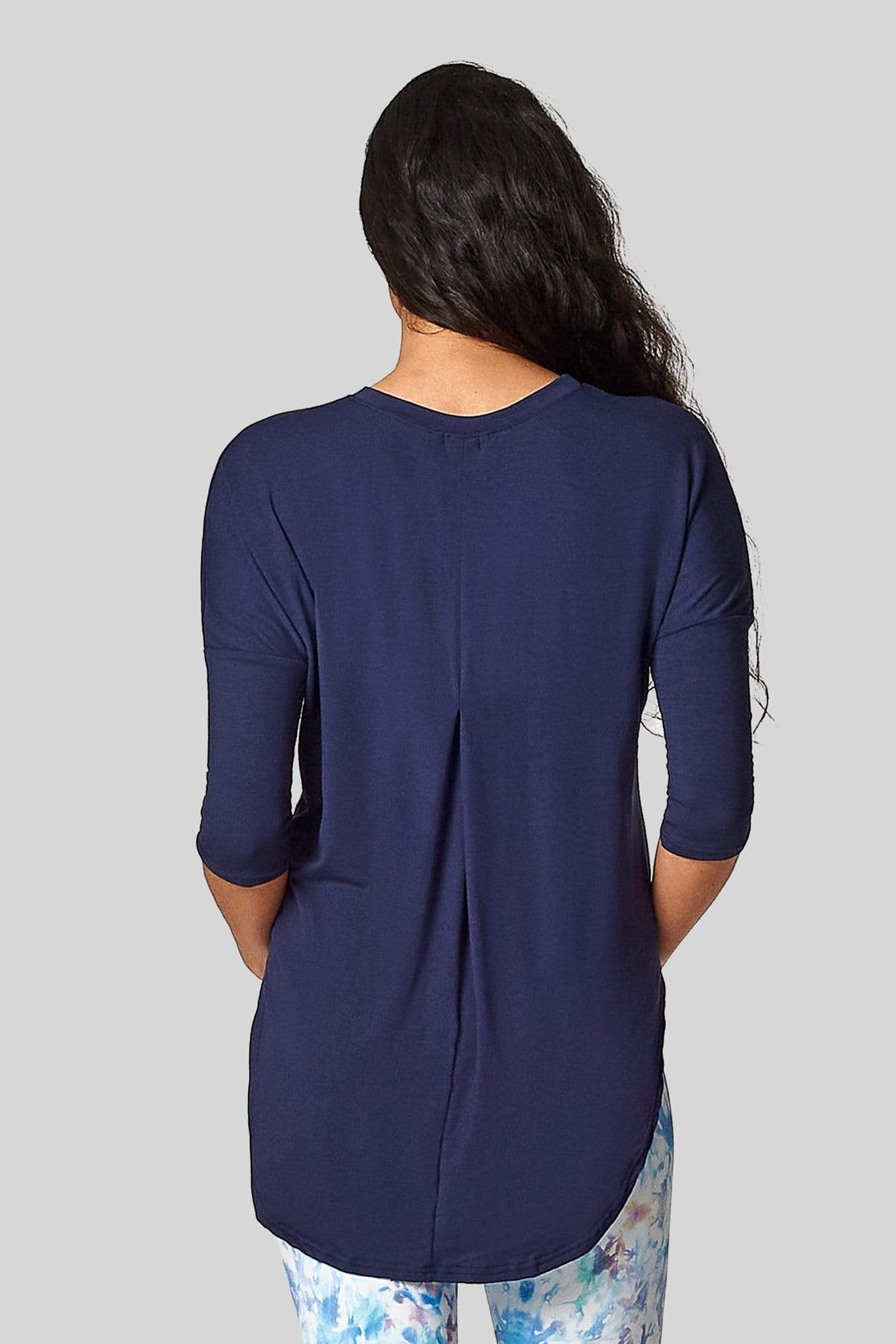 A woman's back faces the camera and she wears a blue 3/4 length tee shirt with a pleat in the back.