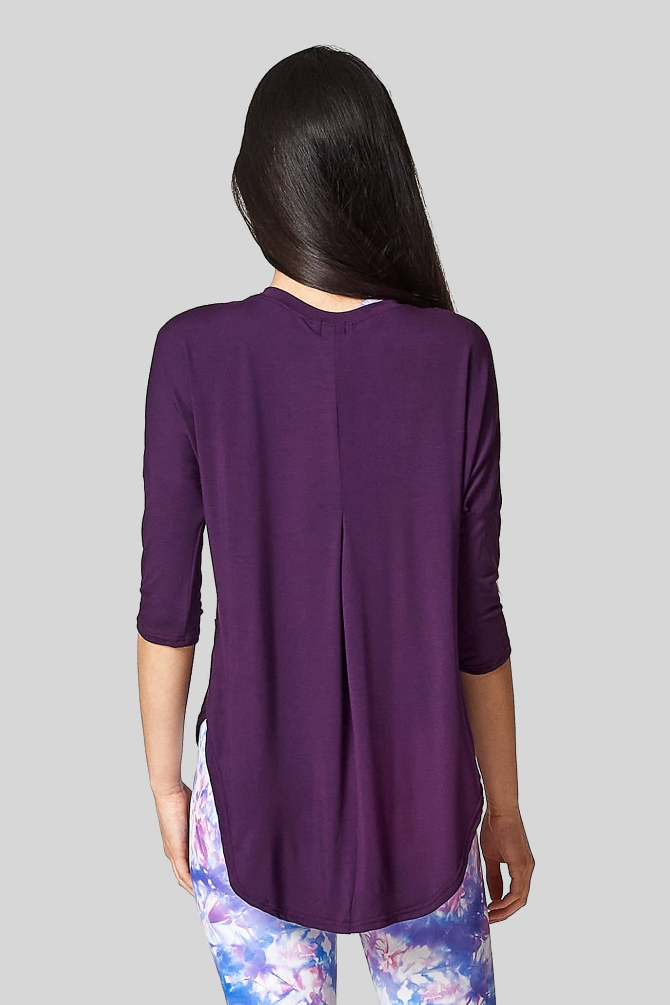 A woman wears a plum t-shirt with a long hem & pleat at the back.