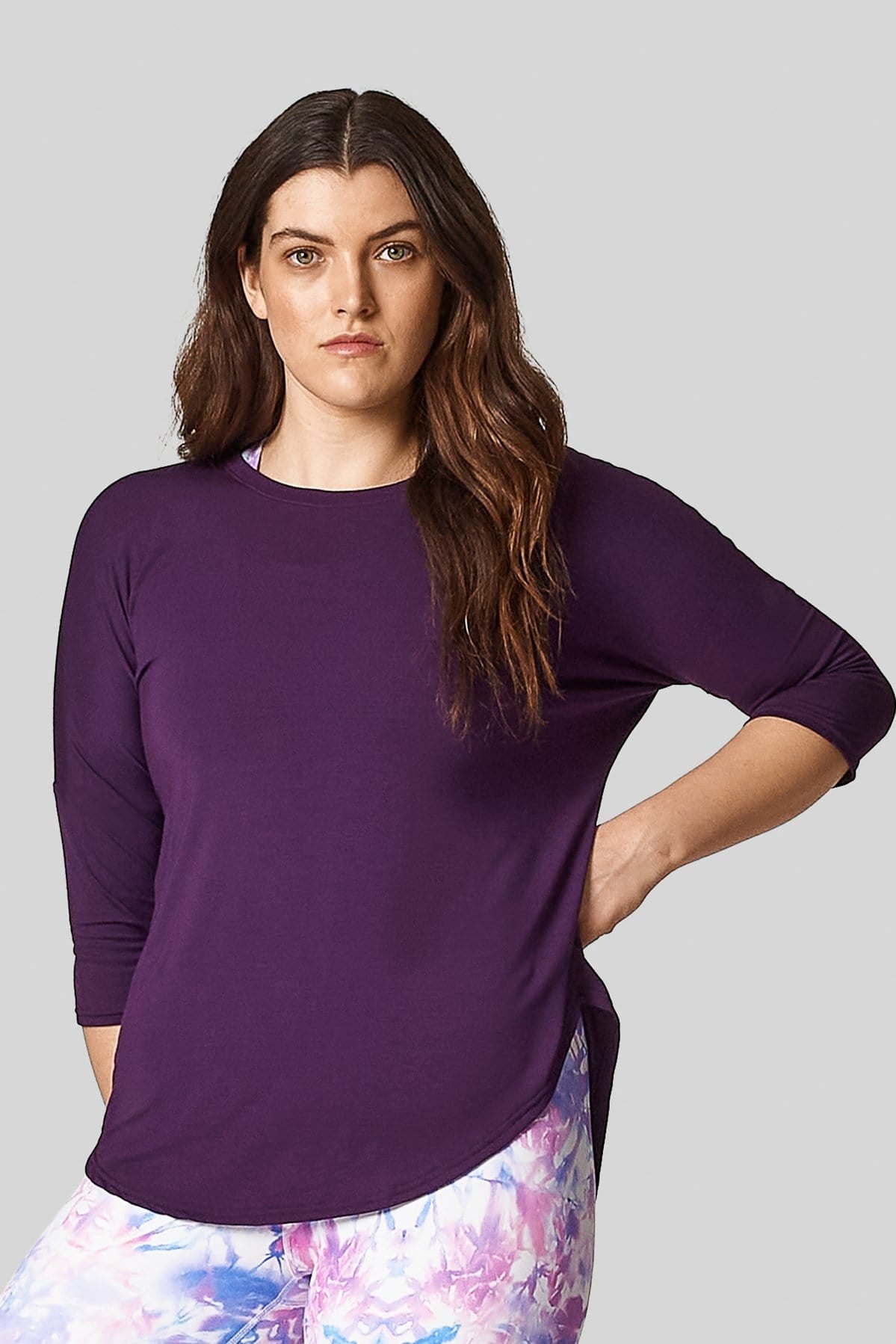 A young woman is modelling a violet shirt with 3/4 length sleeves and printed leggings.