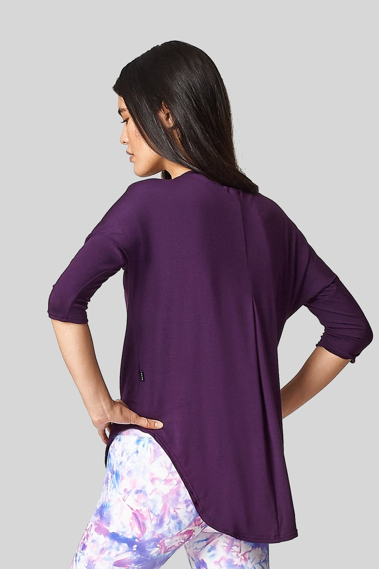 A black haired female is wearing a purple tee-shirt with a scooped hem that is long in the back to cover her bum.