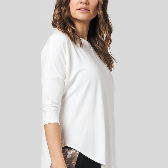 Side of a women wearing a off white 3/4 length sleeve shirt and pocket legging.