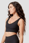 The side profile of a woman modeling a black reversible sports bra.