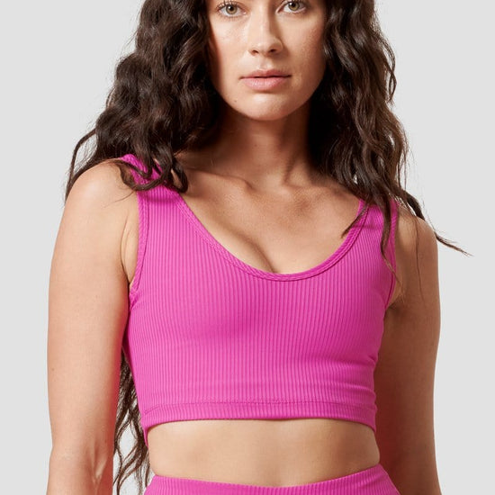 A woman is modeling a hot pink ribbed sports bra. 