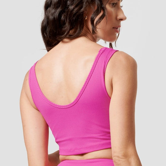 A woman wearing a hot pink reversible top looks over her shoulder.