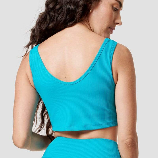 A woman looking over her shoulder models the back of a bright blue ribbed sports bra. 