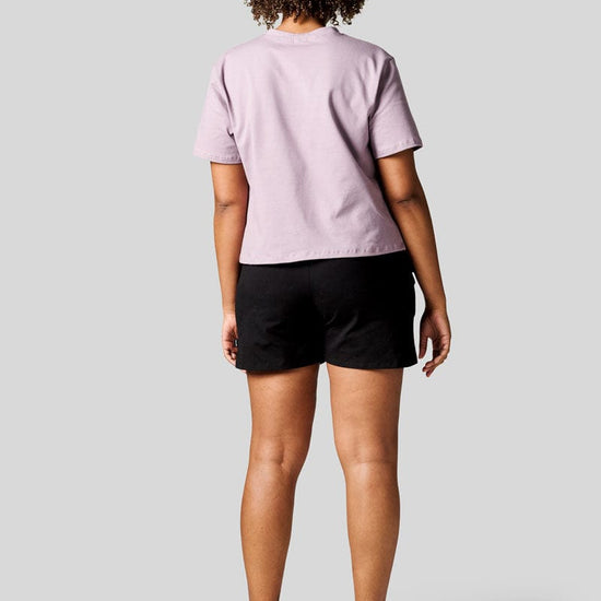 The back of a women wearing a lavender colour tee and black shorts with Nike Air Max