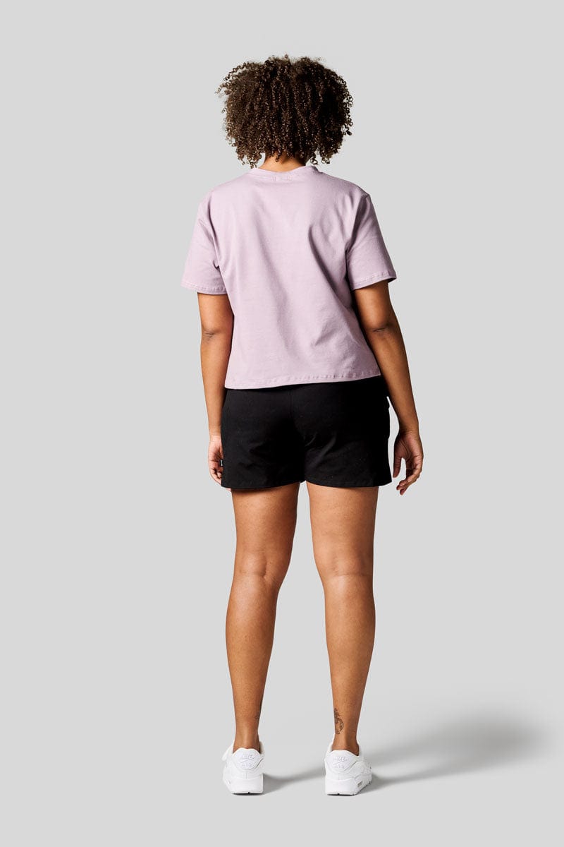 The back of a women wearing a lavender colour tee and black shorts with Nike Air Max