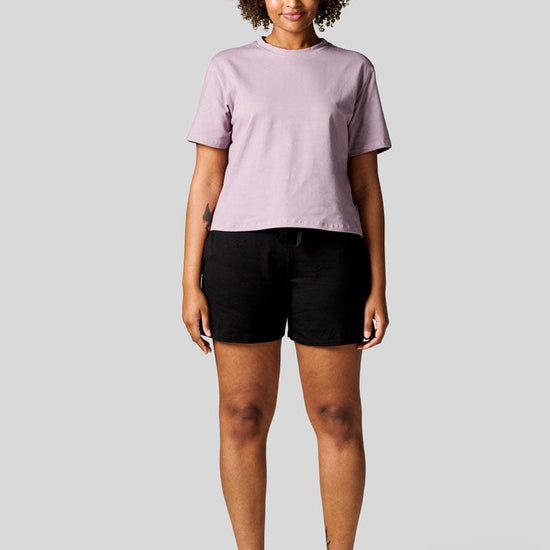 Women standing straight wearing a lavender colour tee and black shorts with Nike Air Max