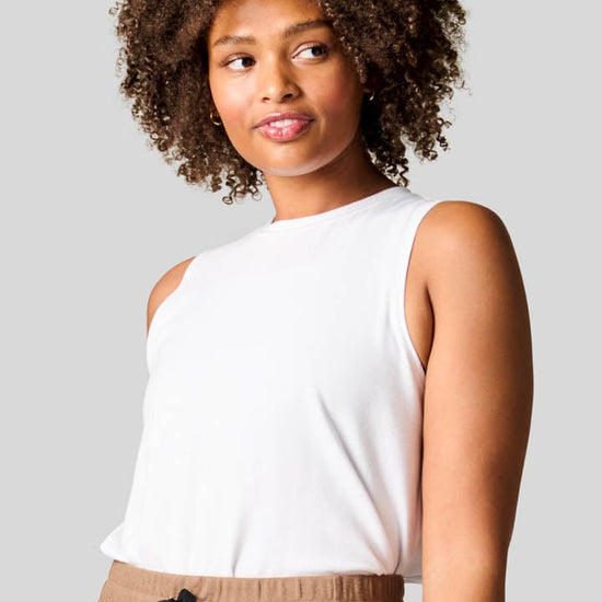 Women wearing a high neck white tank top tucked in brown wide leg pants,