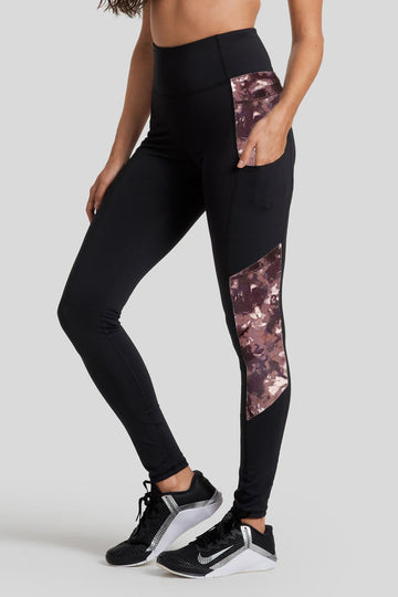A woman stands with her hand in the pocket of her legging. The legging is mainly black & tie dye.