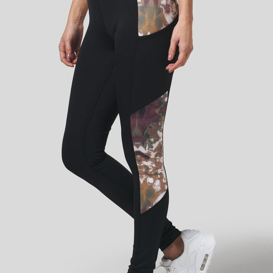 A woman with white Nike Air Max sneakers wears a pair of DAUB pocket leggings in black with a side panel in earthy tie-dye.