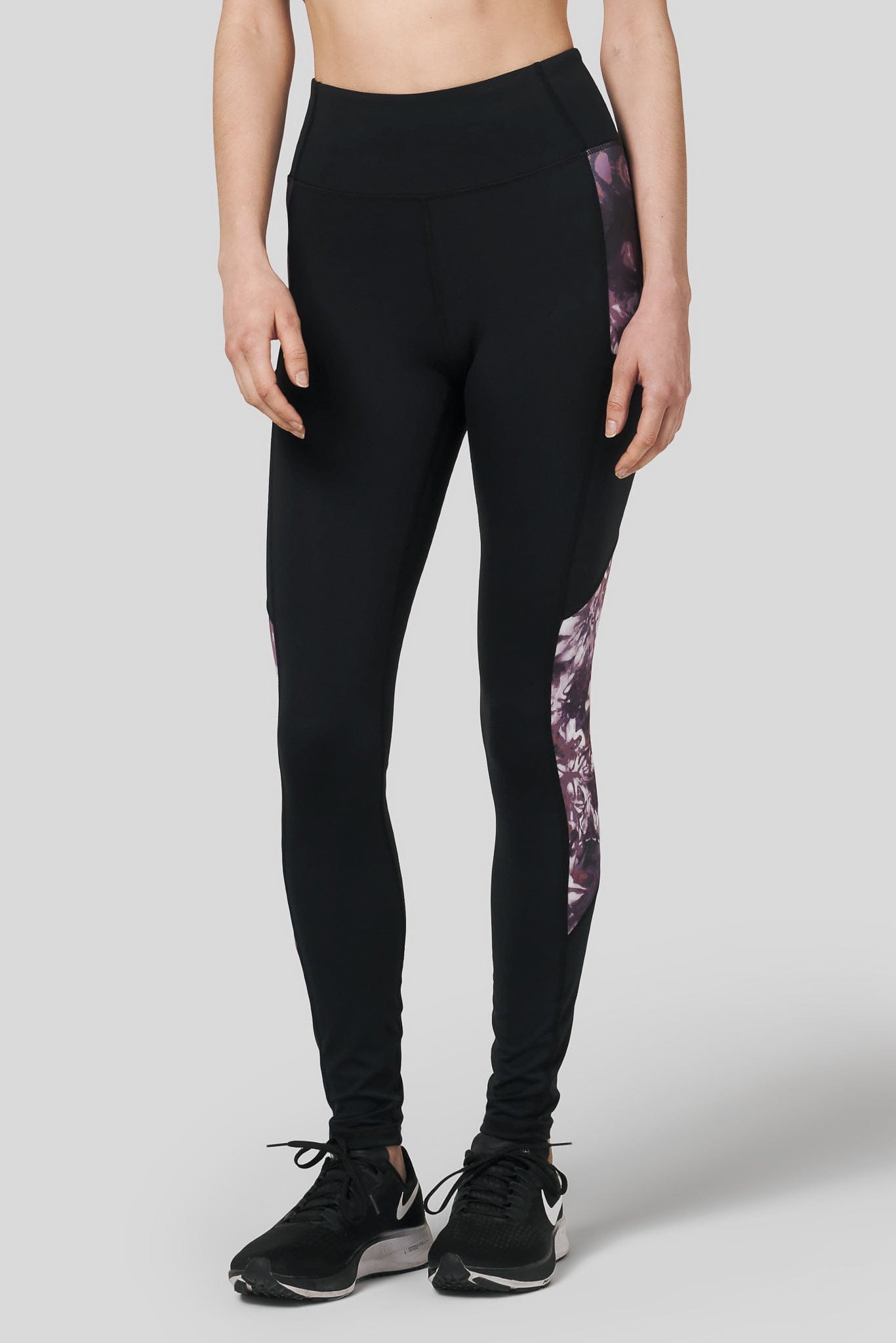 A woman models a black legging with tie dye print and wears nike metcons.