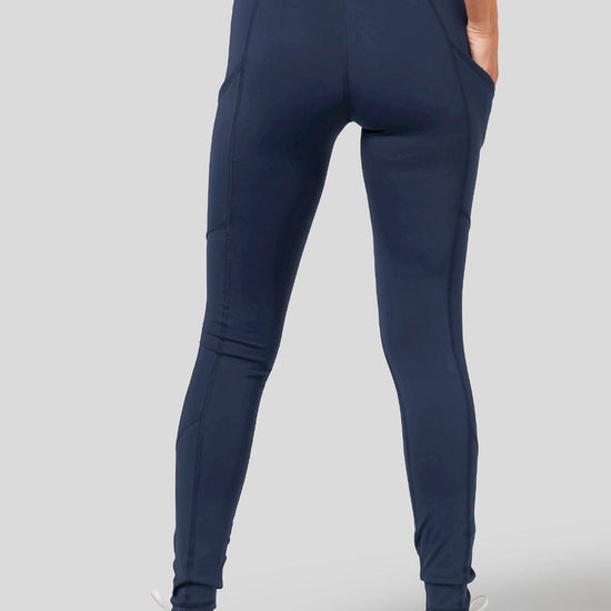 A woman wears a matching activewear set from DAUB in Navy. The leggings have a side pocket to hold your keys & phone.