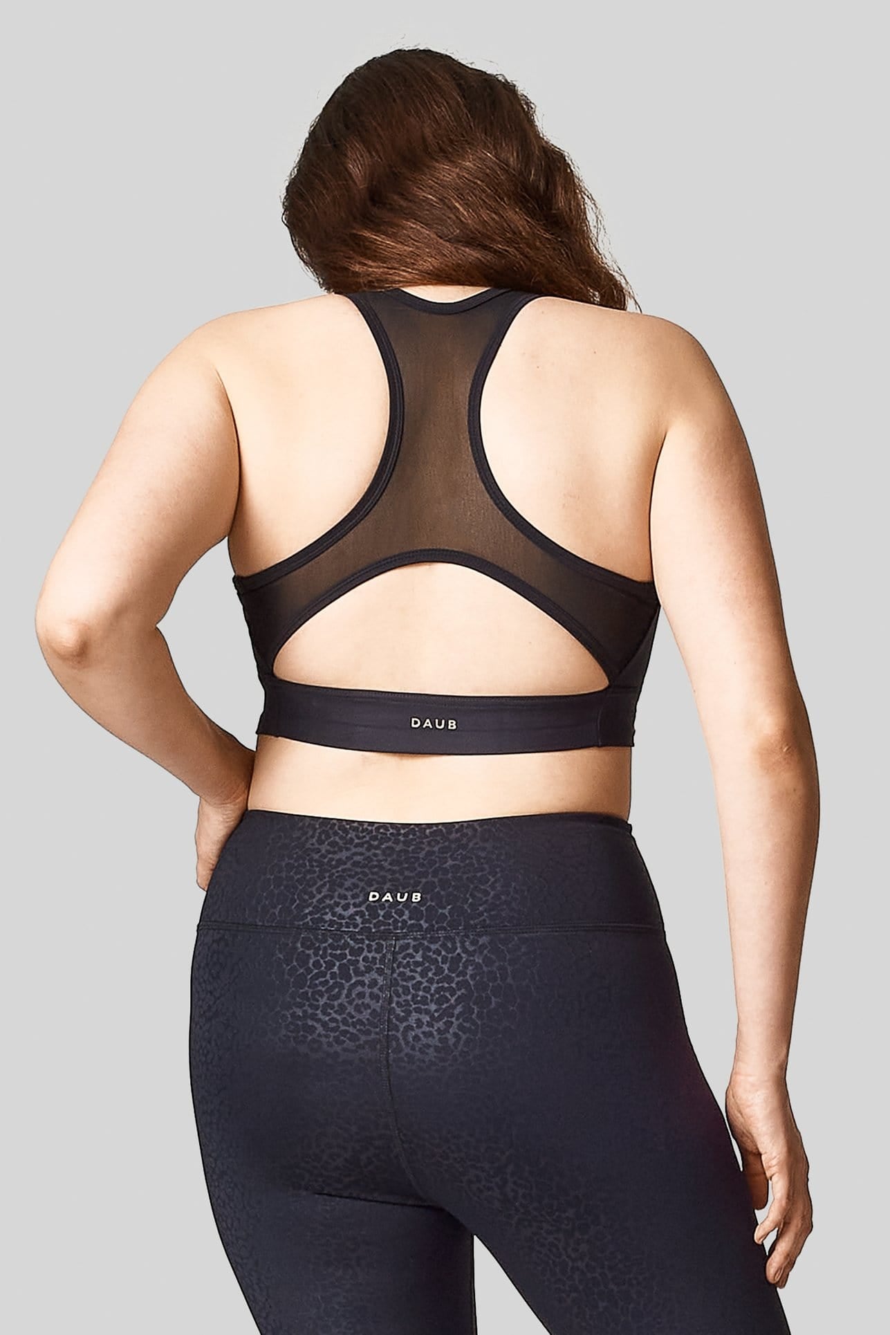Back view of a woman wearing a plain black sports bra with mesh racerback. Paired with cheetah print leggings.