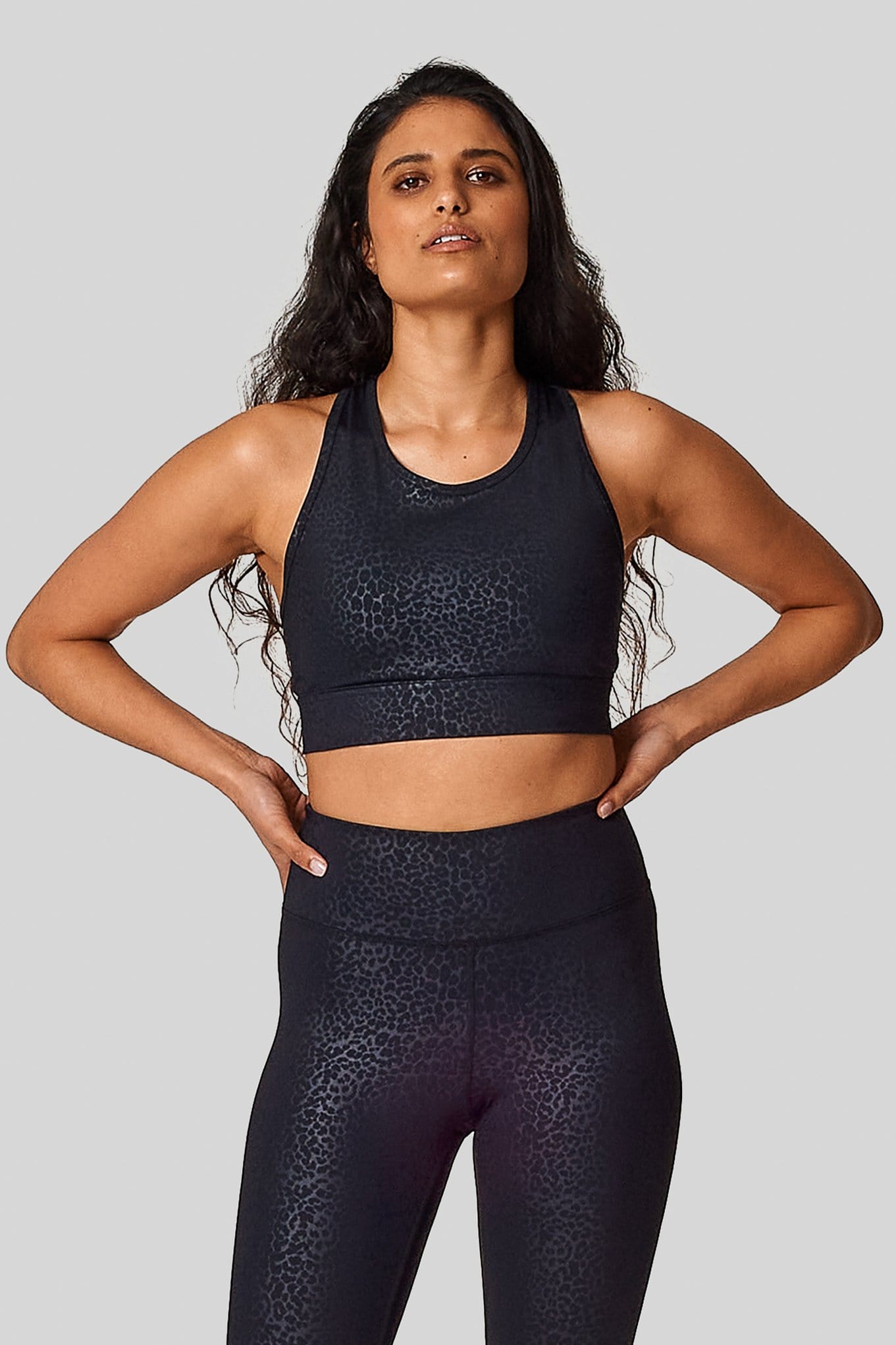 A matching cheetah sports bras & leggings set on a woman with her hands on her hips.