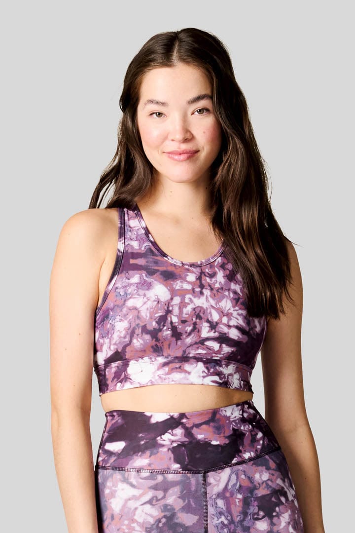 A dark haired woman wears a high neck sports bra in tie dye with a pair of matching Bike Shorts