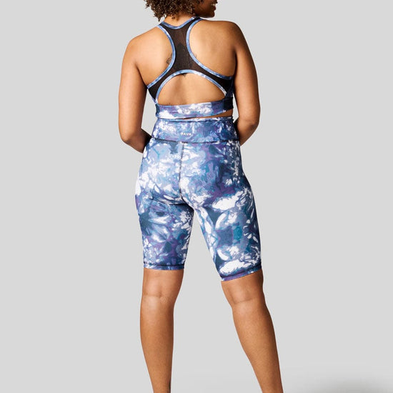 The back of a women wearing blue tie dye bike shorts with matching sports bra and Nike Air Force.