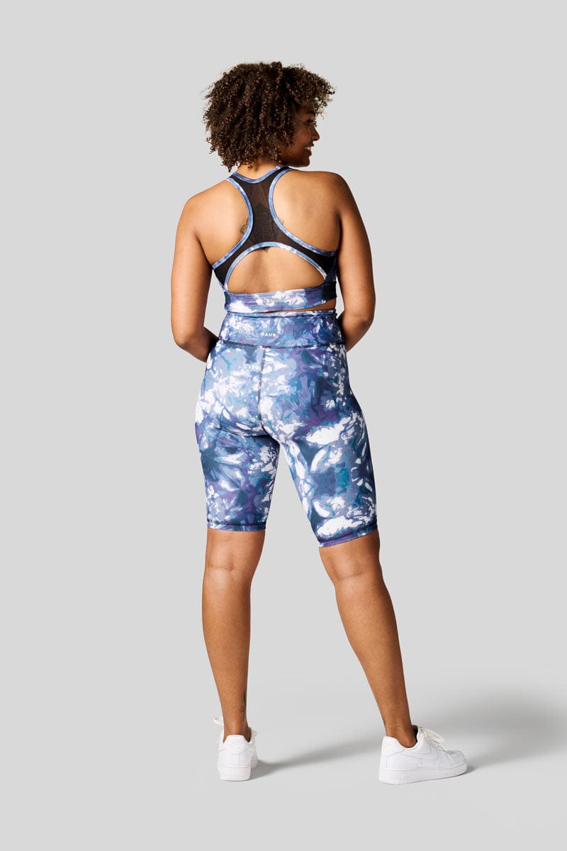 The back of a women wearing blue tie dye bike shorts with matching sports bra and Nike Air Force.