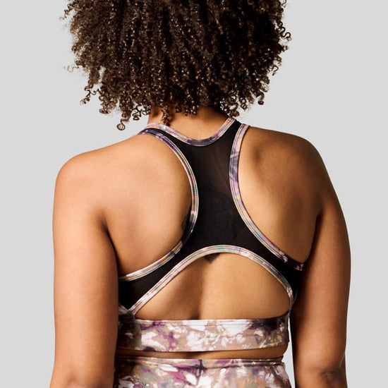 A woman wears a racerback sports bra in a tie-dye print that is made in Canada.