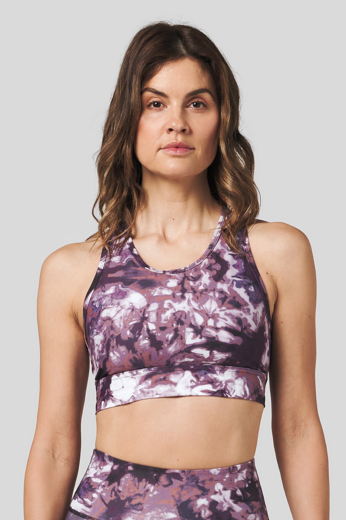 A brunette woman wears a high neck sports bra in a burgundy and white tie-dye print.