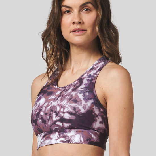 A brunette woman wears a tie dye activewear sports bra and yoga legging set.