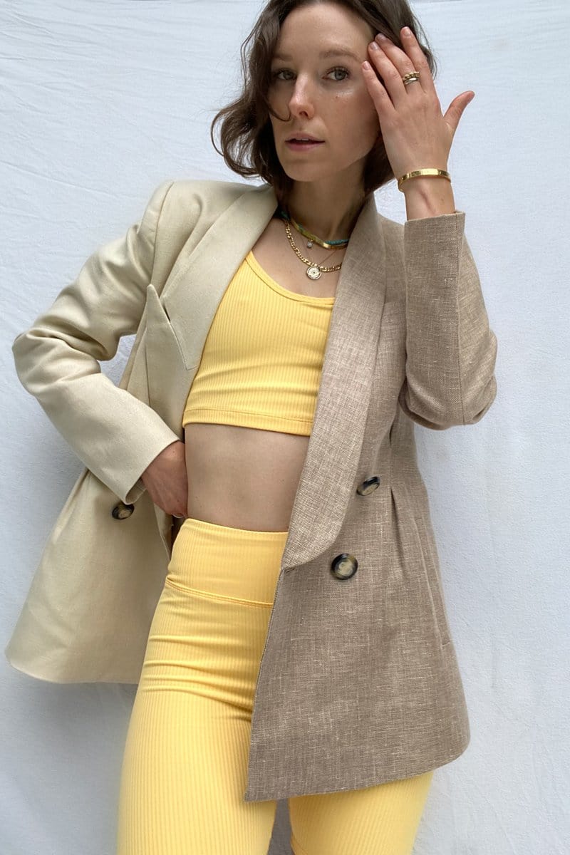 A brunette woman models a yellow sports bra with matching bike shorts and a beige blazer.