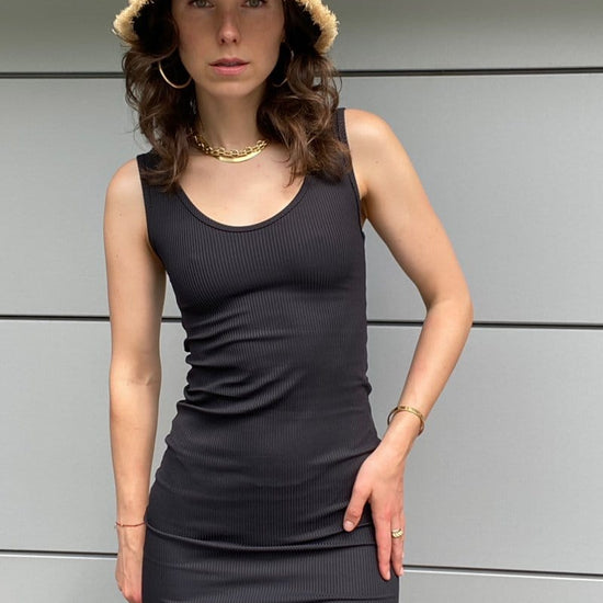 A brunette woman wears a black ribbed bodycon dress paired with a black straw hat.