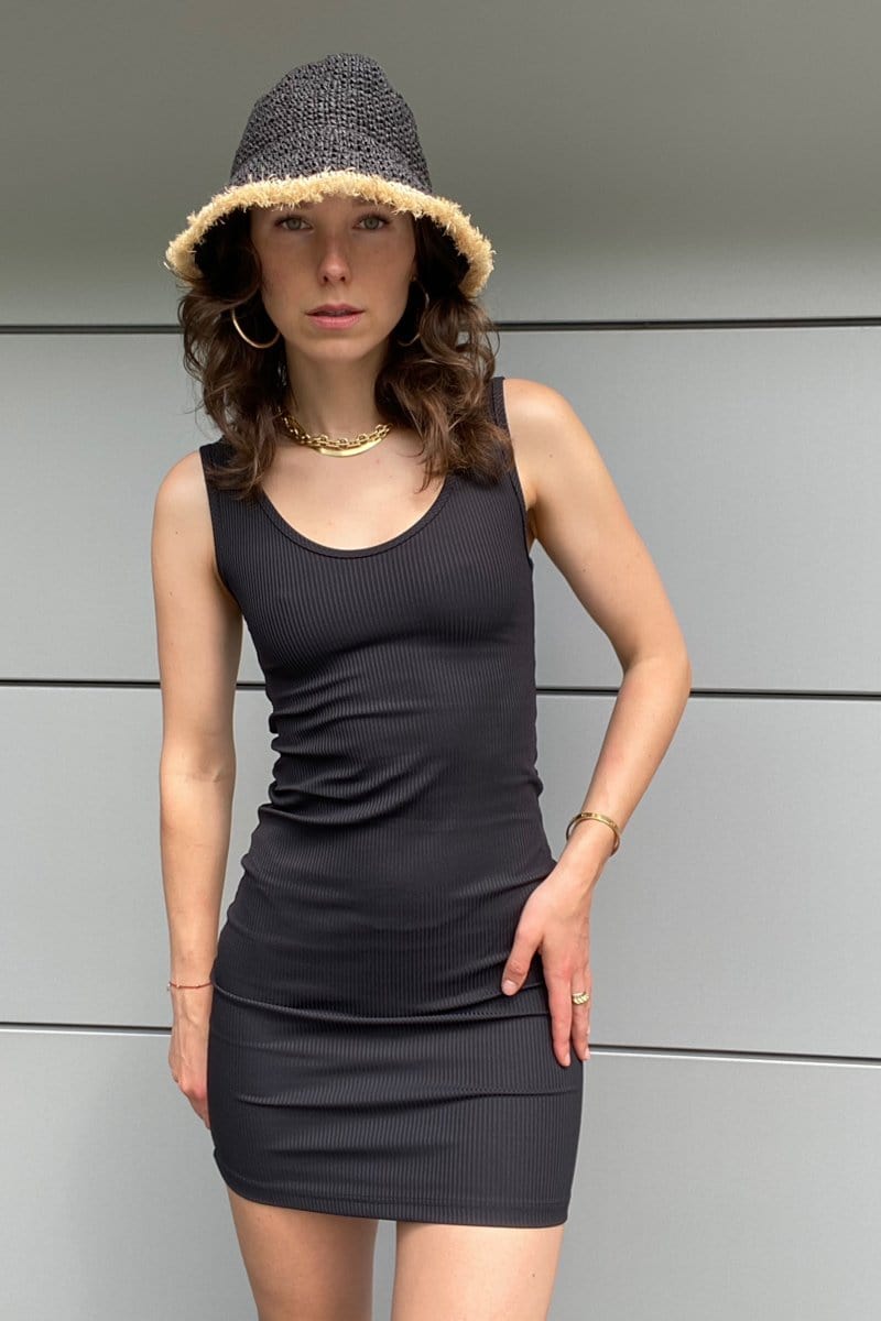 A brunette woman wears a black ribbed bodycon dress paired with a black straw hat.