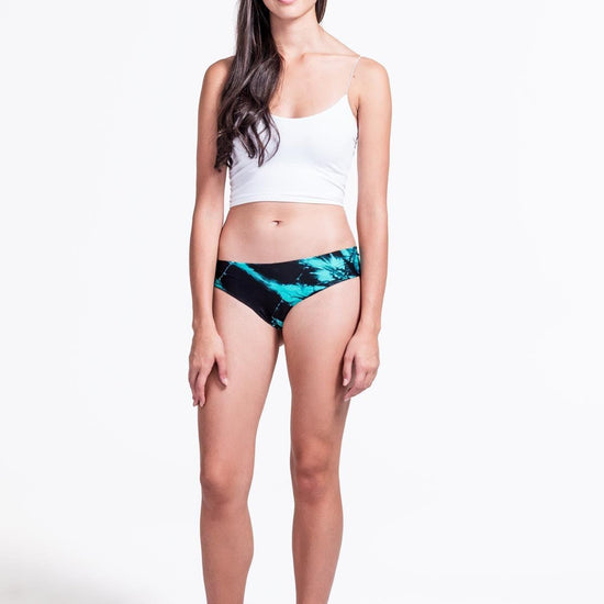 A woman with brown hair models a white tank top and tie-dyed underwear against a white backdrop.